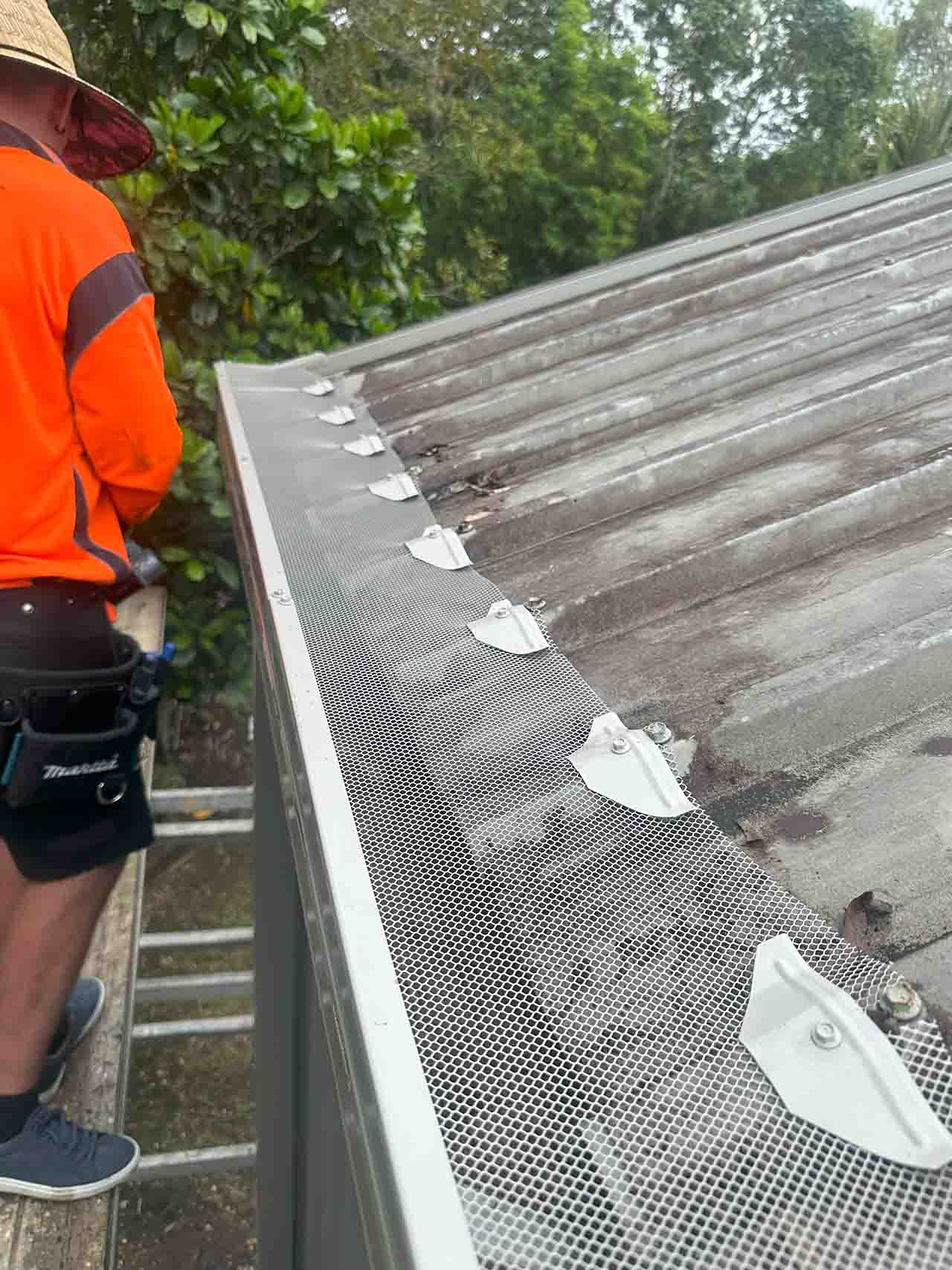 Installer securing aluminium gutter guard mesh to metal roof edge in Smithfield, Cairns
